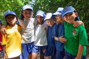 Children in caps holding each other round the shoulder smiling at the camera 